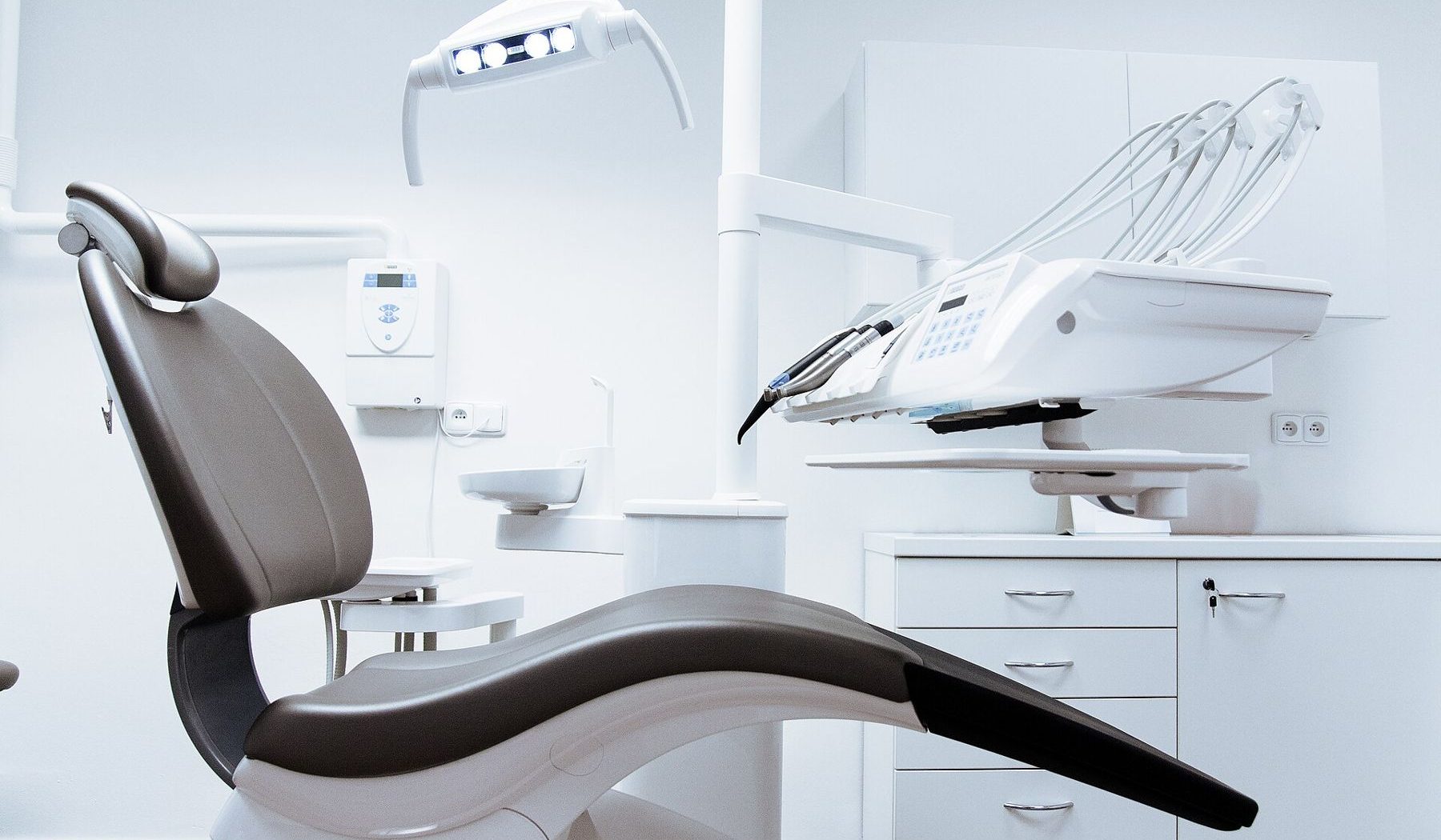 An empty treatment room with a dental chair and overhead light